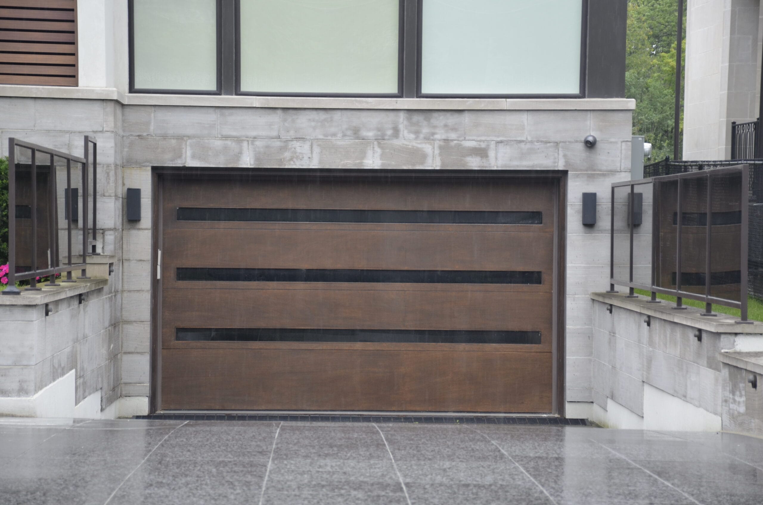 A modern house with a large wooden garage door from Icarus Services on a wet, overcast day.