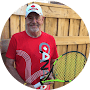 A smiling man wearing a red t-shirt with a 'canada' emblem, holding a yellow tennis racket.